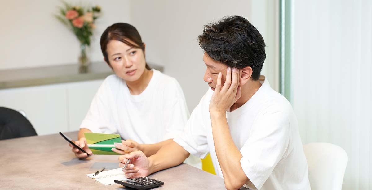 銀行の通帳とスマートフォンを見て考え込む男女