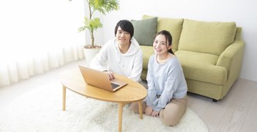 PCが乗っている机のそばで男性と女性が床に座っている画像