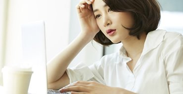 PCを見ながら頬杖をついている女性の画像