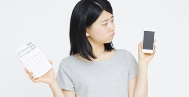 電卓とスマホを持っている女性の画像